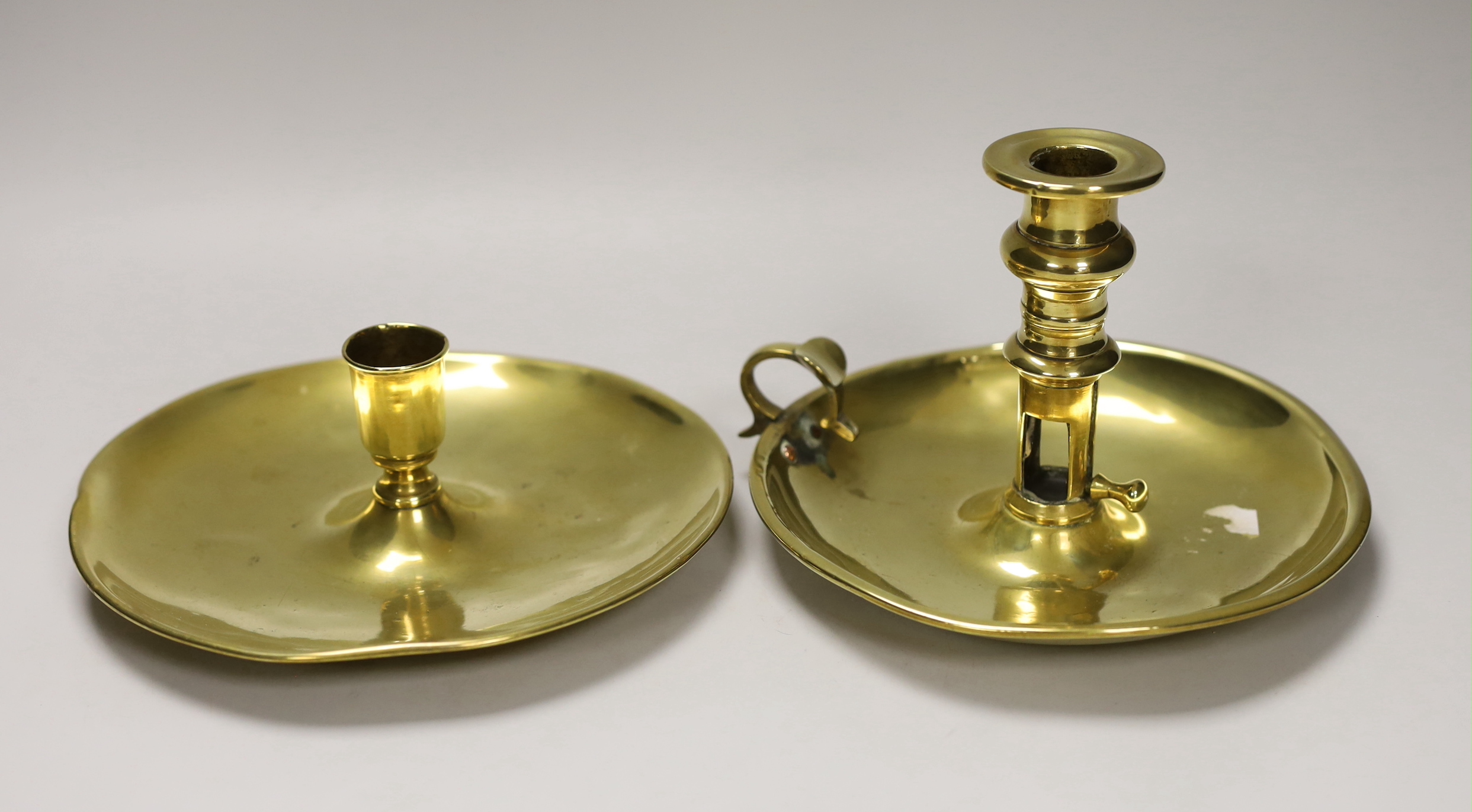 An 18th / 19th century brass saucer candlestick and an 18th century brass chamber candlestick, on circular tray